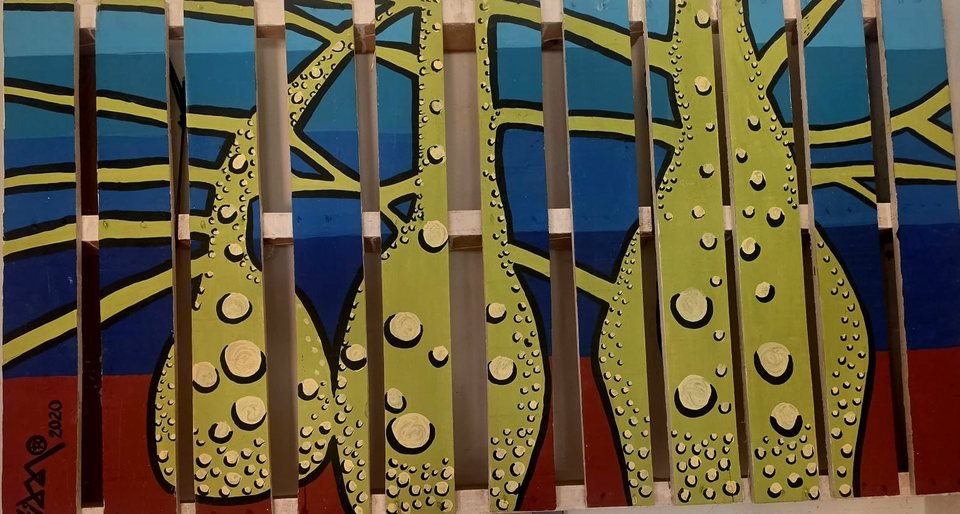Ramas verde lima con burbujas claras y contorno negro, pintadas sobre las tablas de una estiba, con fondo azul y rojo.